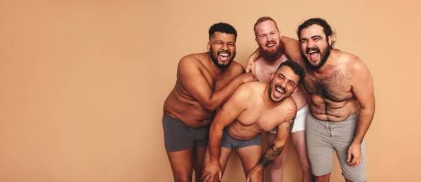 Best friends laughing together with their shirts off Best friends laughing together with their shirts off. Four body positive men having fun while standing together in a studio. Group of self-confident young men feeling comfortable in their natural bodies. semi dress stock pictures, royalty-free photos & images