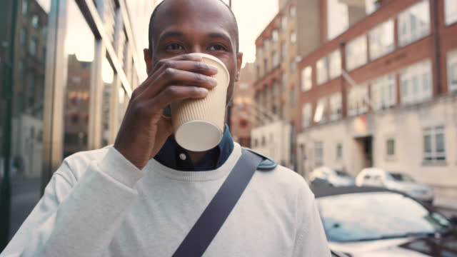 4k video footage of a young businessman drinking coffee and using a cellphone while walking in the city