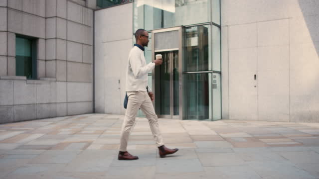 4k video footage of a young businessman drinking coffee while walking in the city