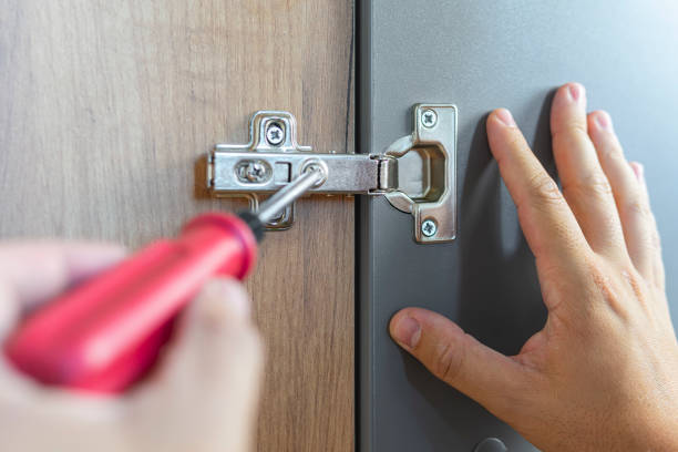 A hand in a screwdriver close-up adjusts the height of the door on cabinet. repairman wooden furniture adjusting. housing assistance concept. person using work tool to assembly or fixing furniture. reparador de muebles de madera ajustando. concepto de asistencia a la vivienda. persona que utiliza la herramienta de trabajo para ensamblar o arreglar muebles. una mano en un primer plano de destornillador ajusta la altura de la puerta en el gabinete.