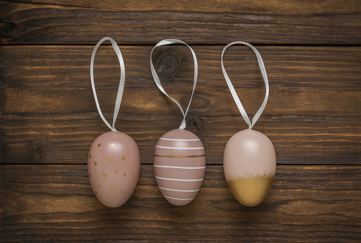 Three Easter eggs with ribbons on a wooden background. Minimal Easter concept. Flat lay.