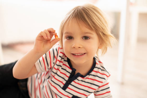 mignon petit enfant, garçon en bas âge, mangeant alfa oméga 3 pilules de vitamines de suplement pour enfants à la maison - vitamin d capsule fish oil yellow photos et images de collection