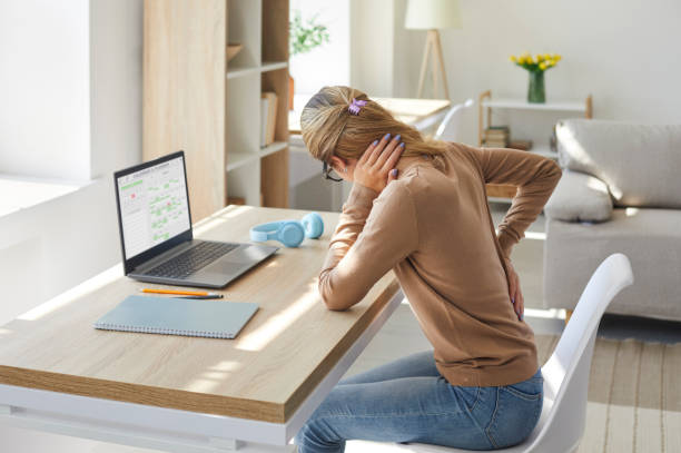 la mujer que trabaja en postura sentada en su computadora portátil sufre de dolor de espalda - bajo posición descriptiva fotografías e imágenes de stock