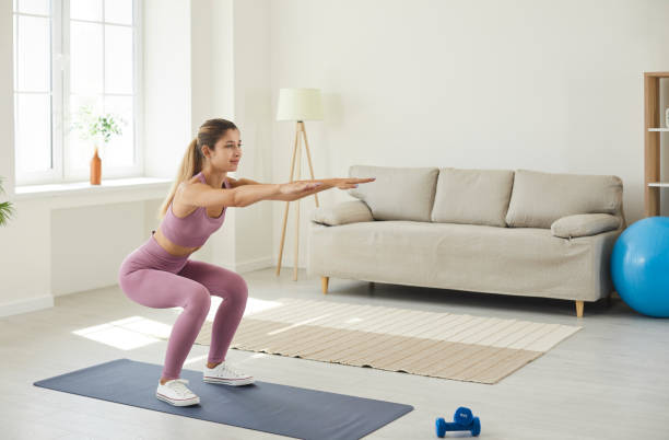 istock Young enduring woman trains at home doing deep squats with her arms outstretched. 1388927079