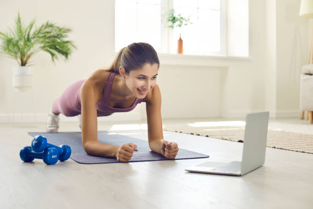 istock Young athletic woman performs plank exercise while communicating with coach via video link. 1388927083