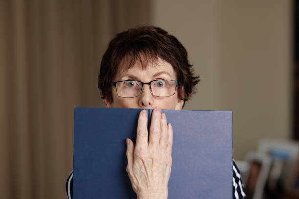 Woman peering over the top of a book. Senior woman gets a shock from what she was just read. short story stock pictures, royalty-free photos & images