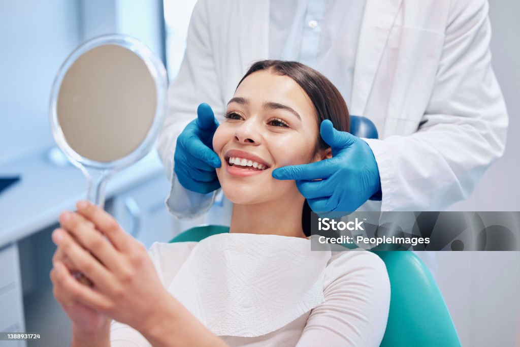 Shot of a young woman checking her results in the dentists office No better feeling than this Dentist Stock Photo