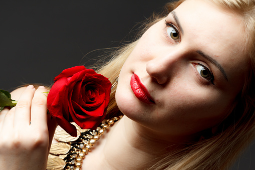 Beautiful happy girl holds red rose close to face and looks at camera. High quality photo