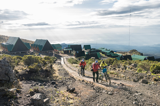 Three male mountainbikers are pushing their mountainbikes uphill from their latest camp Horombo Huts (3.720 mt., 12.205 ft.) towards the summit region of Mt. Kilimanjaro (5.895 mt., 19.341 ft.) on the Marangu route.\nCanon EOS 760D, 1/200, f/8, 18 mm.