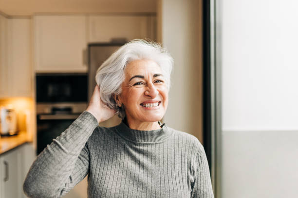 alegre mujer mayor sonriendo a la cámara en casa - white hair fotografías e imágenes de stock