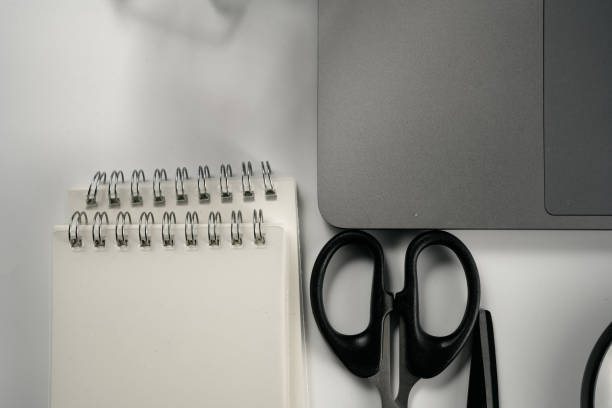 Laptop, magnifying glass, scissors, shopping cart and notebook on white background board