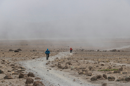 Two male mountainbikers are riding and pushing the bicycles uphill in the desert like saddle region between Mt. Mawenzi (5.148 mt., 16.890 ft.) and Mt. Kilimanjaro (5.895 mt., 19.341 ft.) on the Marangu route at an altitude around 4.400 mt.(14.436 ft.).\nCanon EOS 760D, 1/200, f/11, 118 mm.