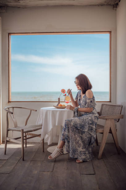 A woman traveler sits by the window relaxing and enjoying her vacation at the sea cafe. stock photo