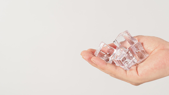 Hand is holding ice cubes on white background.
