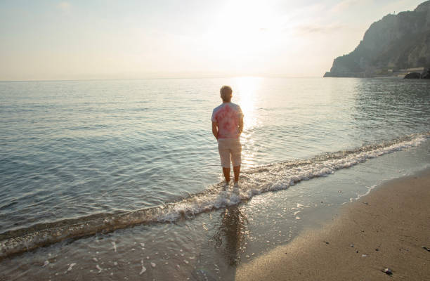istock Man wades in sea shallows, looking off 1388936076