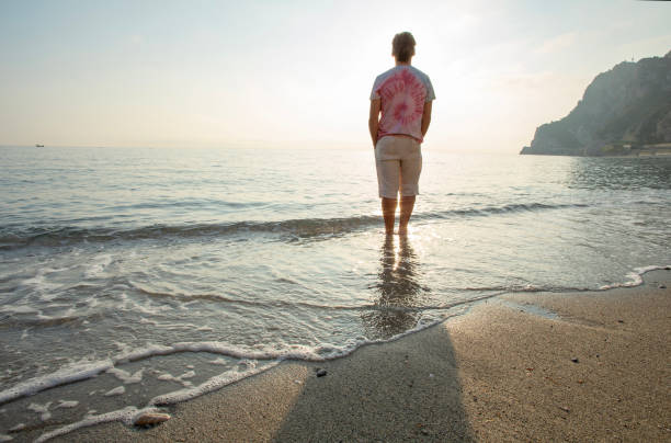 istock Man wades in sea shallows, looking off 1388936078