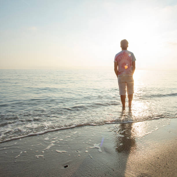 istock Man wades in sea shallows, looking off 1388936079