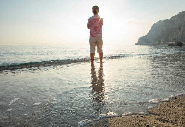istock Man wades in sea shallows, looking off 1388936140