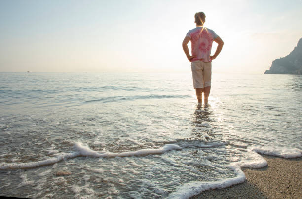 istock Man wades in sea shallows, looking off 1388936143