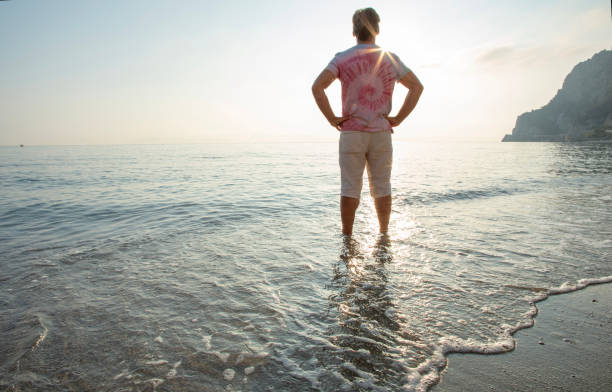 istock Man wades in sea shallows, looking off 1388936176