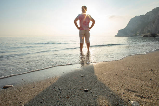 istock Man wades in sea shallows, looking off 1388936196
