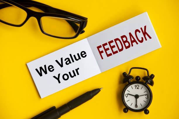 Text on notepad with reading glasses, pen and alarm clock on yellow background - We value your feedback. Conceptual Text on notepad with reading glasses, pen and alarm clock on yellow background - We value your feedback. constructive feedback stock pictures, royalty-free photos & images
