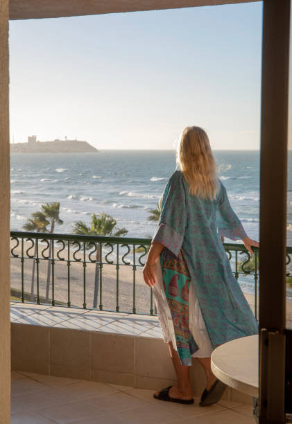 istock Woman enjoys view from elevated terrace, beach and sea below 1388936359