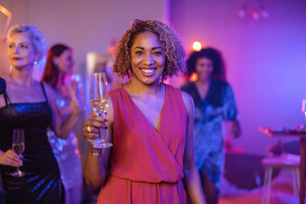 une femme afro-américaine mature tenant sa coupe de champagne et souriant pour la caméra - champagne flute champagne black wineglass photos et images de collection