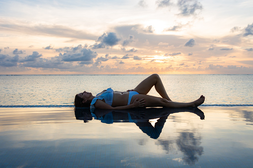 Woman lying down on a infinity pool at sunset in Maldive Islands