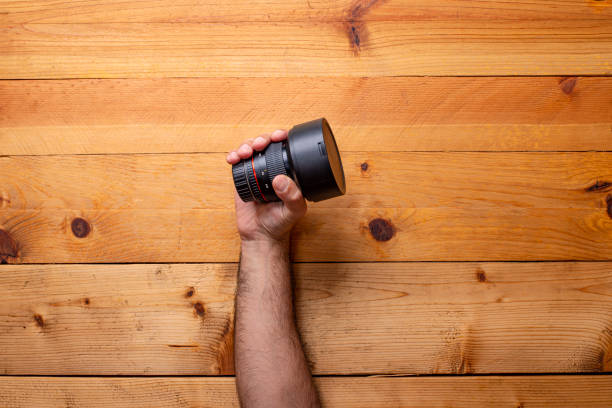 hand grabbing camera lens on light wood background - Labor Day