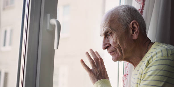 istock Sad senior pensioner looking through window glass 1388938915