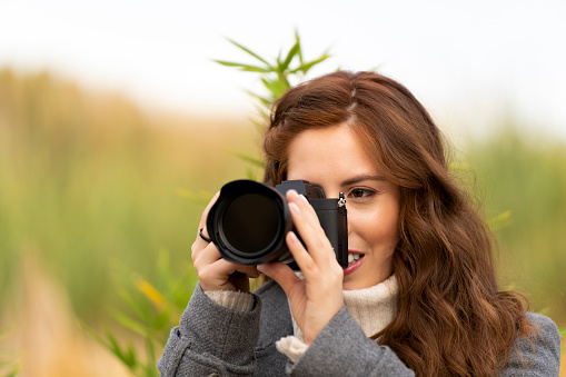 Red-haired young woman taking a picture with her photo camera outside