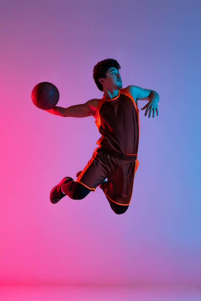 istock Young energetic man playing basketball isolated on gradient pink blue studio background in neon light. Youth, hobby, motion, activity, sport concepts. 1388940528