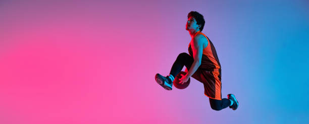 istock Young energetic man playing basketball isolated on gradient pink blue studio background in neon light. Youth, hobby, motion, activity, sport concepts. 1388940529
