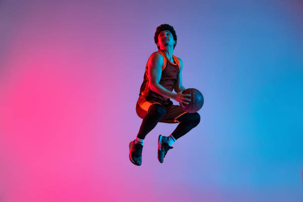 istock Young energetic man playing basketball isolated on gradient pink blue studio background in neon light. Youth, hobby, motion, activity, sport concepts. 1388940533