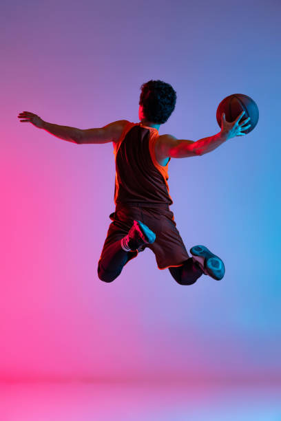 istock Young energetic man playing basketball isolated on gradient pink blue studio background in neon light. Youth, hobby, motion, activity, sport concepts. 1388940535