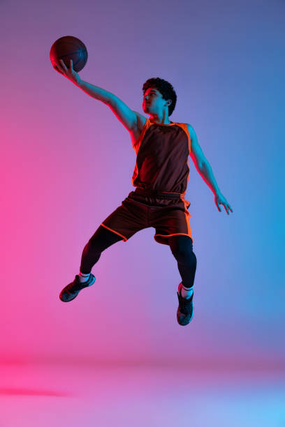 istock Young energetic man playing basketball isolated on gradient pink blue studio background in neon light. Youth, hobby, motion, activity, sport concepts. 1388940536