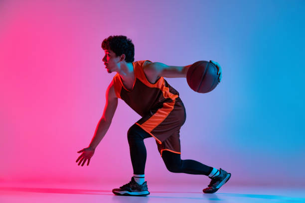 istock Sportive man playing basketball isolated on gradient pink blue studio background in neon light. Youth, hobby, motion, activity, sport concepts. 1388940538