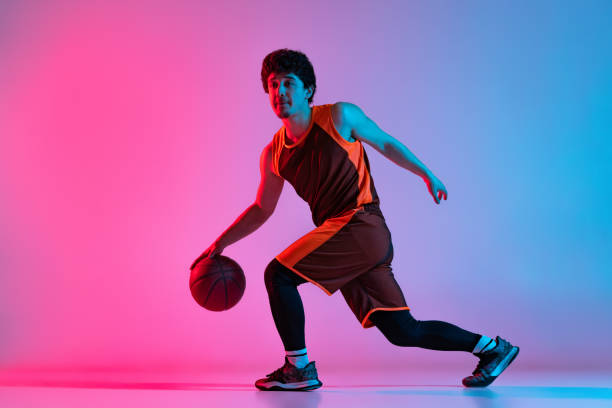 istock Sportive man playing basketball isolated on gradient pink blue studio background in neon light. Youth, hobby, motion, activity, sport concepts. 1388940539