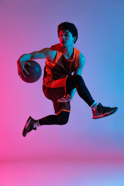 istock Young energetic man playing basketball isolated on gradient pink blue studio background in neon light. Youth, hobby, motion, activity, sport concepts. 1388940540