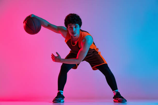 istock Young energetic man playing basketball isolated on gradient pink blue studio background in neon light. Youth, hobby, motion, activity, sport concepts. 1388940541