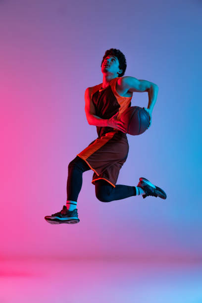 istock Sportive man playing basketball isolated on gradient pink blue studio background in neon light. Youth, hobby, motion, activity, sport concepts. 1388940548