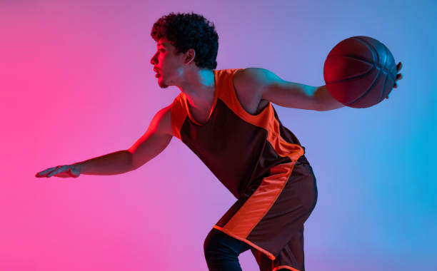 istock Young energetic man playing basketball isolated on gradient pink blue studio background in neon light. Youth, hobby, motion, activity, sport concepts. 1388940551