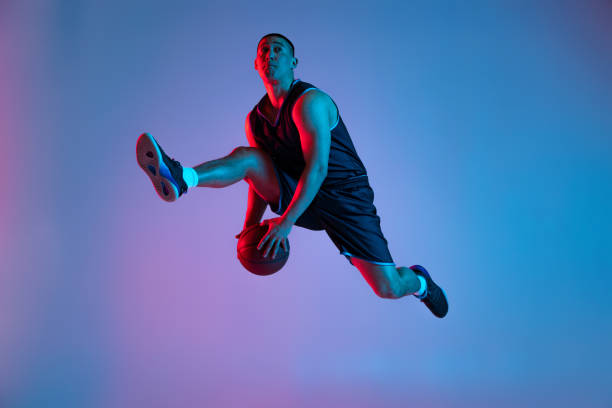 giovane sportivo che gioca a basket isolato sullo sfondo blu dello studio in luce al neon. giovani, hobby, movimento, attività, concetti sportivi. - streetball basketball sport men foto e immagini stock