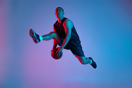 istock Young sportive man playing basketball isolated on blue studio background in neon light. Youth, hobby, motion, activity, sport concepts. 1388940556