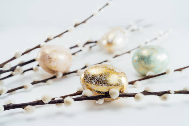 istock Blooming pussy willow branches and golden eggs in different patterns and colors on the white background. Minimalist, Modern Happy easter card. Selective focus, copy space. 1388944935