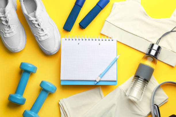 istock Flat lay composition with sportswear, notebook and dumbbells on yellow background. Gym workout plan 1388949313