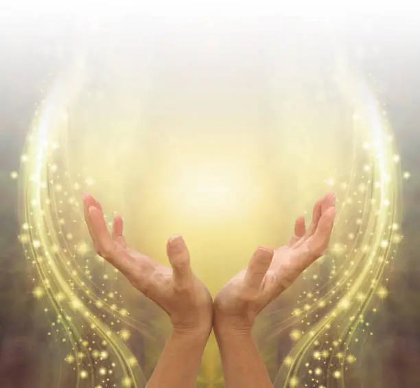 female cupped hands reaching up into bright white light against spiritual sparkling  background graduated from white to gold to brown and copy space