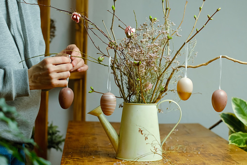 Female hands decorating Easter flower arrangement. Spring cozy home interior.