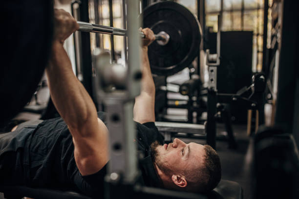 Man doing bench press One man, fit man training with on exercise machine in gym alone. Barbell stock pictures, royalty-free photos & images